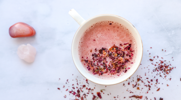 Pink Moon Milk Ayurvedic Recipe in a mug on quartz countertop surrounded by rose petals and crystals