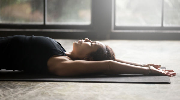 The Ultimate Guide to CBD and Back Pain. Image of Woman lying on yoga mat stretching her back